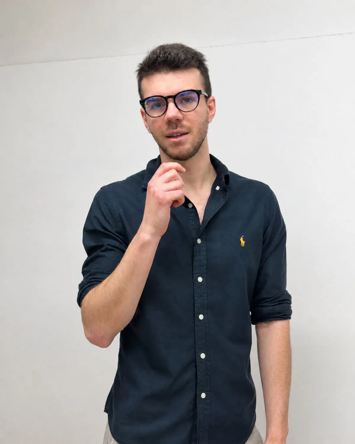 Lorenzo Chirdo, camicia blu scuro e occhiali dalla montatura scura, ritratto in piedi su fondo chiaro